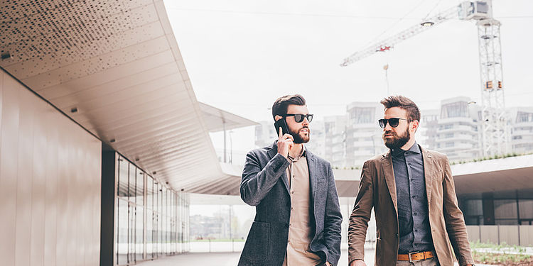 two contemporary businessman walking talking smart phone